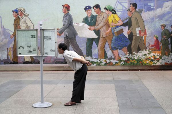 Пассажир метро в Пхеньяне читает газету на стенде - Sputnik Таджикистан