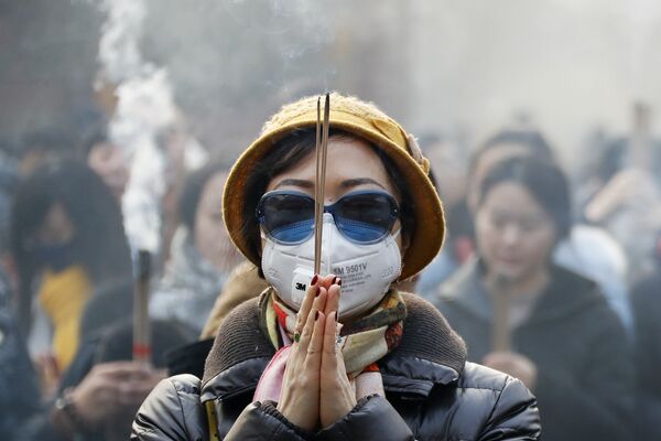 Женщина в маске и солнцезащитных очках во время молитвы в первый день Нового года в Пекине - Sputnik Таджикистан