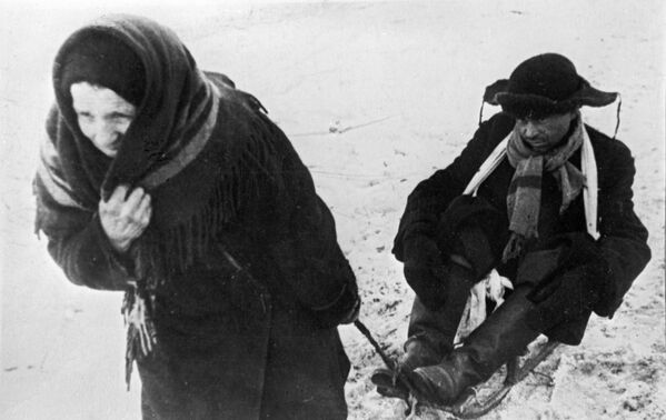 Жители блокадного Ленинграда: женщина везет ослабевшего от голода мужа на санках - Sputnik Таджикистан