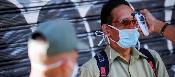 Мужчине в защитной лицевой маске измеряют температуру - Sputnik Таджикистан