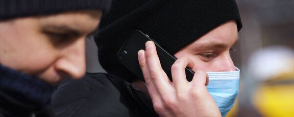 Молодой человек в медицинской маске разговаривает по телефону - Sputnik Таджикистан
