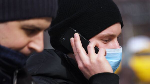 Молодой человек в медицинской маске разговаривает по телефону - Sputnik Таджикистан