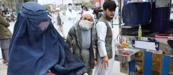 Сотрудники афганской национальной службы закупок распыляют дезинфицирующее средство на руки женщины - Sputnik Тоҷикистон