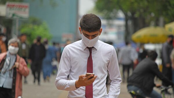 Мужчина в маске смотрит на телефон - Sputnik Тоҷикистон