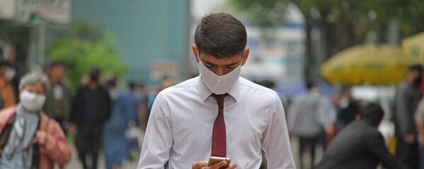 Мужчина в маске смотрит на телефон - Sputnik Тоҷикистон