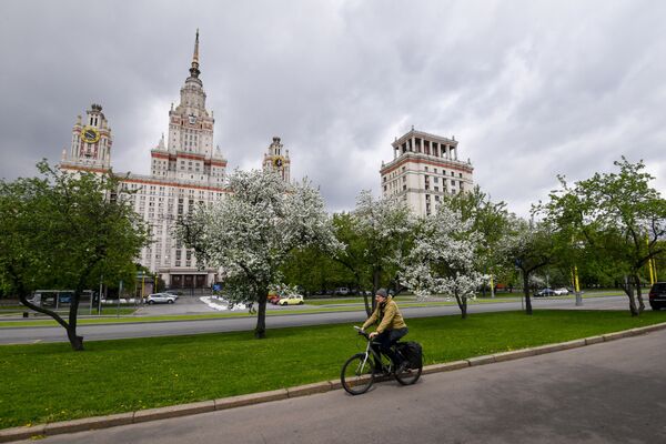 Велосипедист на фоне цветущих деревьев у здания МГУ в Москве - Sputnik Таджикистан
