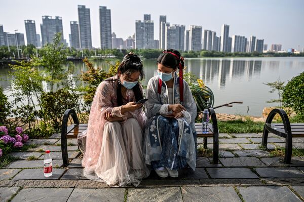 Молодые женщины в масках и в традиционных костюмах на скамейке в парке Уханя, Китай - Sputnik Таджикистан