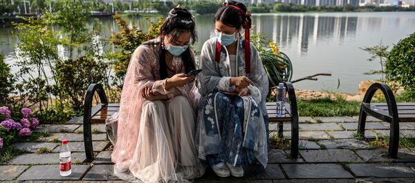 Молодые женщины в масках и в традиционных костюмах на скамейке в парке Уханя, Китай - Sputnik Тоҷикистон