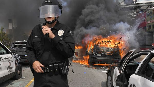 Полицейский Лос-Анджелеса на фоне горящей машины во время протестов  - Sputnik Таджикистан