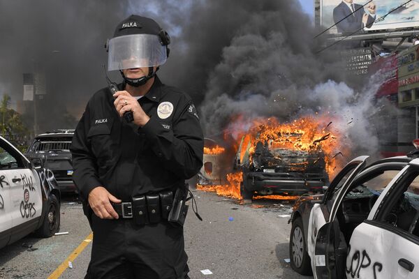 Полицейский Лос-Анджелеса на фоне горящей машины во время протестов  - Sputnik Таджикистан