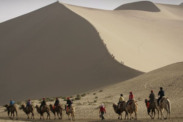 Туристы катаются на верблюдах на краю пустыни, которая угрожает поглотить древний китайский город Дуньхуан  - Sputnik Таджикистан