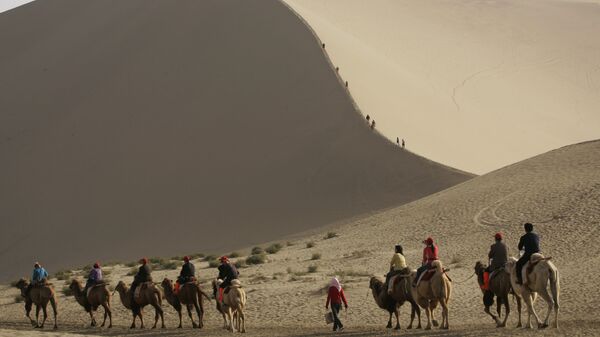 Туристы катаются на верблюдах на краю пустыни, которая угрожает поглотить древний китайский город Дуньхуан  - Sputnik Таджикистан