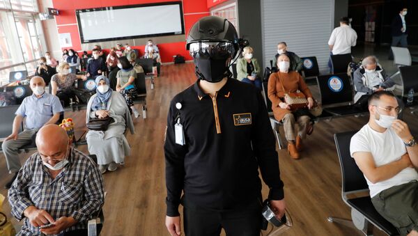 Сотрудник службы безопасности в тепловизионном шлеме следит за пассажирами, ожидающими посадки на рейс в аэропорту Стамбула - Sputnik Тоҷикистон