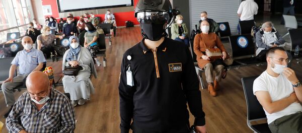 Сотрудник службы безопасности в тепловизионном шлеме следит за пассажирами, ожидающими посадки на рейс в аэропорту Стамбула - Sputnik Тоҷикистон