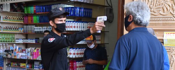 Сотрудник охраны рынка Мехргон проверяет температуру у посетителя Сотрудник охраны рынка Мехргон проверяет температуру у посетителя - Sputnik Тоҷикистон