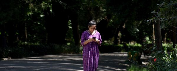 Девушка смотрит в телефон, прогуливаясь в саду Ирам - Sputnik Таджикистан